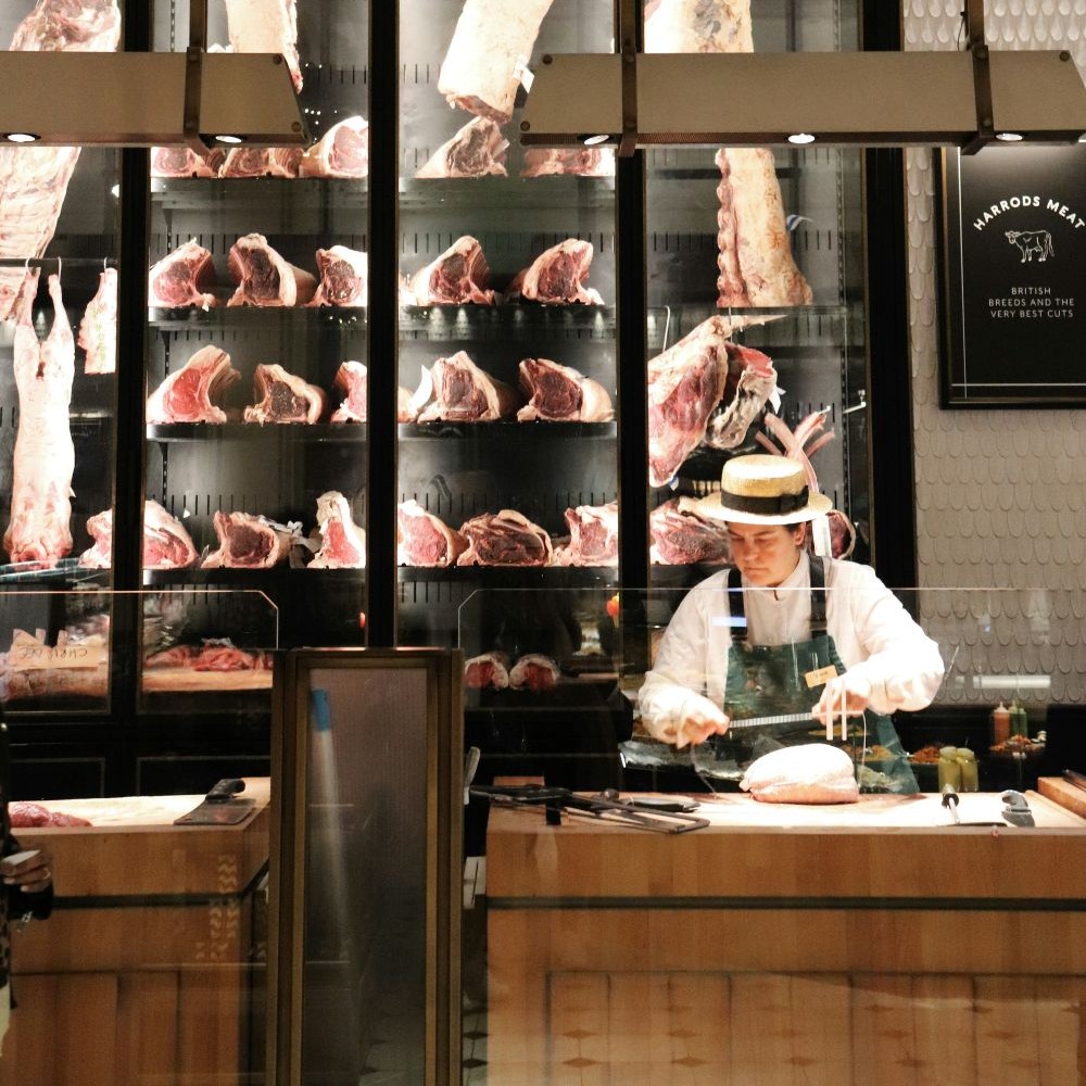 Butcher preparing cuts behind a specialist meat counter.